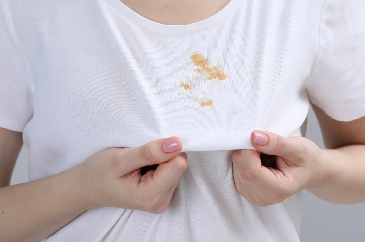 Une femme debout portant un t-shirt blanc avec une tache visible sur le tissu.